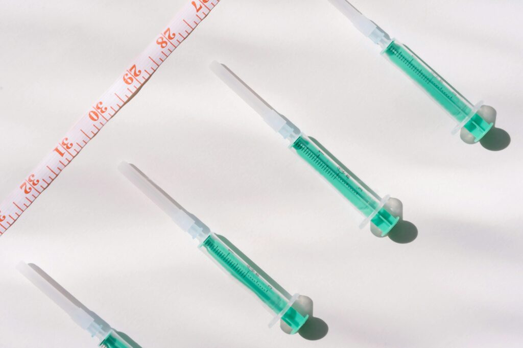 Top view of green filled syringes and measuring tape on a white background, emphasizing healthcare themes.